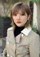 A woman wearing a beige trench coat and a black turtle neck sweater.